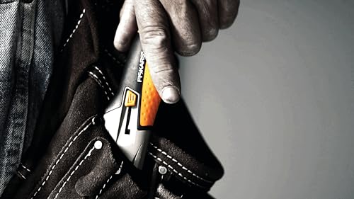 Fiskars Cuttermesser mit ergonomischem Griff und CarbonMax Klinge, ideal für präzise Schneidarbeiten, abgebildet in der Hand eines Nutzers auf dunklem Hintergrund.